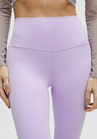 Leggings a vita alta di un leggero colore viola, realizzati in tessuto elasticizzato, con una superficie liscia e cuciture piatte per comfort e supporto.