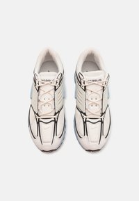 Bílé sportovní boty s prodyšným svrškem z síťoviny, černým prošíváním a šedými akcenty. Mají texturovanou gumovou podrážku a systém šněrování.