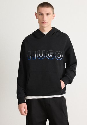 Svart hettegenser med et stort, stilisert "HUGO"-logo i blå gradient. Har en lomme foran og justerbar hette. Myk stoff, avslappet passform.