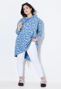 Ljusblå tunika med vitt "STAR"-textmönster, långa ärmar, rundad nederkant, tillsammans med vita figurnära byxor och svarta plattformssandaler.