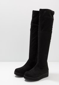 Czarne kozaki za kolano wykonane z miękkiego zamszu. Masywna podeszwa na platformie z teksturowanym bieżnikiem. Bezszwowy design bez widocznych elementów z metalu.