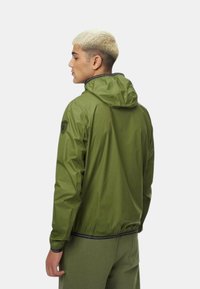 Giacca leggera verde con cappuccio, caratterizzata da una finitura testurizzata e polsini elasticizzati. Patch con logo sulla spalla sinistra.