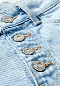 Lyseblåt denimstof med fire metalknapper, der er justeret lodret, hver sikret med orange syning.