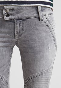 Jeans de mezclilla gris con un diseño ajustado, que cuentan con un cierre de botón, detalles desgastados y paneles texturizados en los laterales.