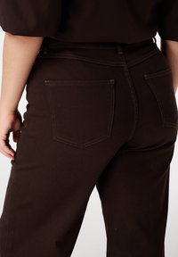 Bruine jeans met hoge taille en een aansluitende pasvorm, voorzien van twee achterzakken en contrasterende stikselpatronen.