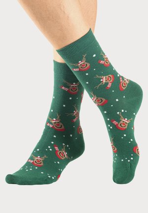 Grüne Socken mit einem wiederholten Rentier-Muster, das einen roten Hut und einen Schal trägt, mit weißen Sprenkeln, die Schnee darstellen. Weiche, gestrickte Textur.