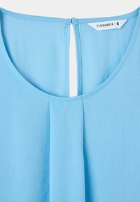 Top azzurro chiaro con scollatura rotonda e dettaglio a oblò sul retro. Il materiale sembra liscio con una leggera trama. L'etichetta mostra "Terranova S."