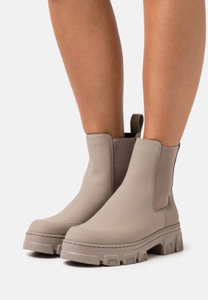 Beige Chelsea boots with elastic side panels and a chunky rubber sole. Smooth finish with textured accents on the sides.