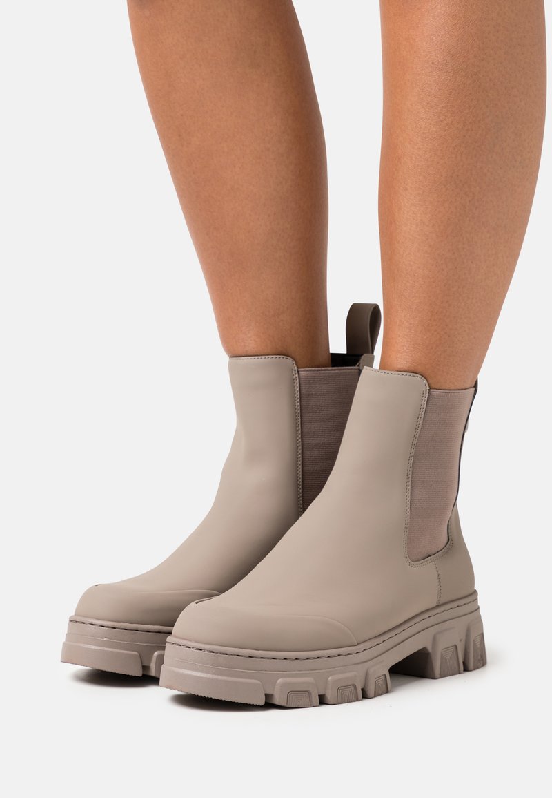Beige Chelsea boots with elastic side panels and a chunky rubber sole. Smooth finish with textured accents on the sides.