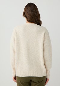 Pull en tricot beige avec une texture douce, des poignets et un ourlet côtelés, présentant une coupe légèrement oversized et un col rond.