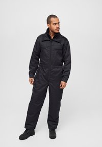 Black jumpsuit featuring a zip front, long sleeves, and two chest pockets. Material appears durable with a smooth texture and elastic waistband.