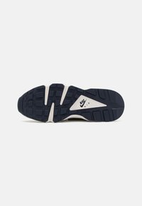 Nike Air trenirke s teksturiranim, tamnoplavim gumenim đonom, koji ima bijelu srednju podlogu i vidljivi logo na području pete. Geometrijski uzorak na đonu.