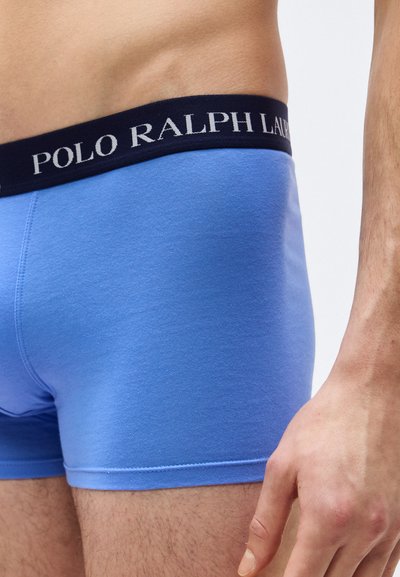 Κοντινό πλάνο ενός ατόμου που φορά φωτεινά γαλάζια ανδρικά εσώρουχα τύπου μποξέρ με μαύρη μέση που φέρει την ένδειξη "Polo Ralph Lauren".