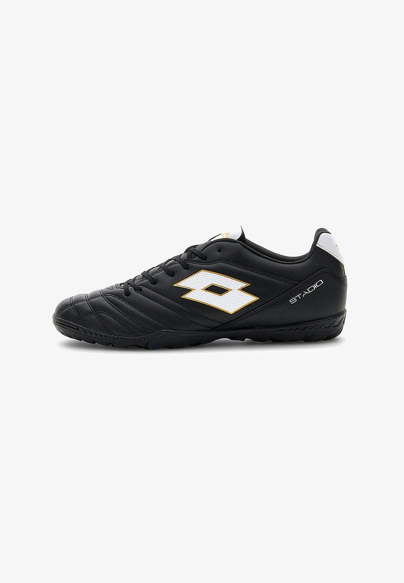 Chaussure de football noire à coupe basse avec logo blanc et doré, semelle texturée et inscription « STADIO » sur le talon, vue de côté sur fond blanc.