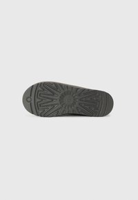 Semelle de chaussure en caoutchouc noir avec une surface texturée présentant un motif en rayons de soleil, conçue pour l'adhérence et la durabilité. Bords lisses et talon arrondi.