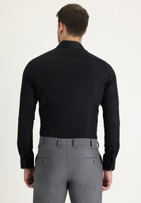 Camisa negra de manga larga con una textura suave, combinada con pantalones grises de corte a medida que presentan un diseño sencillo y bolsillos discretos.