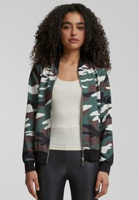 Tarnjacke in Camouflage-Design mit grünen, braunen und weißen Mustern. Rippbündchen an den Ärmeln und am Saum, durchgehender Reißverschluss und leichtes Material.