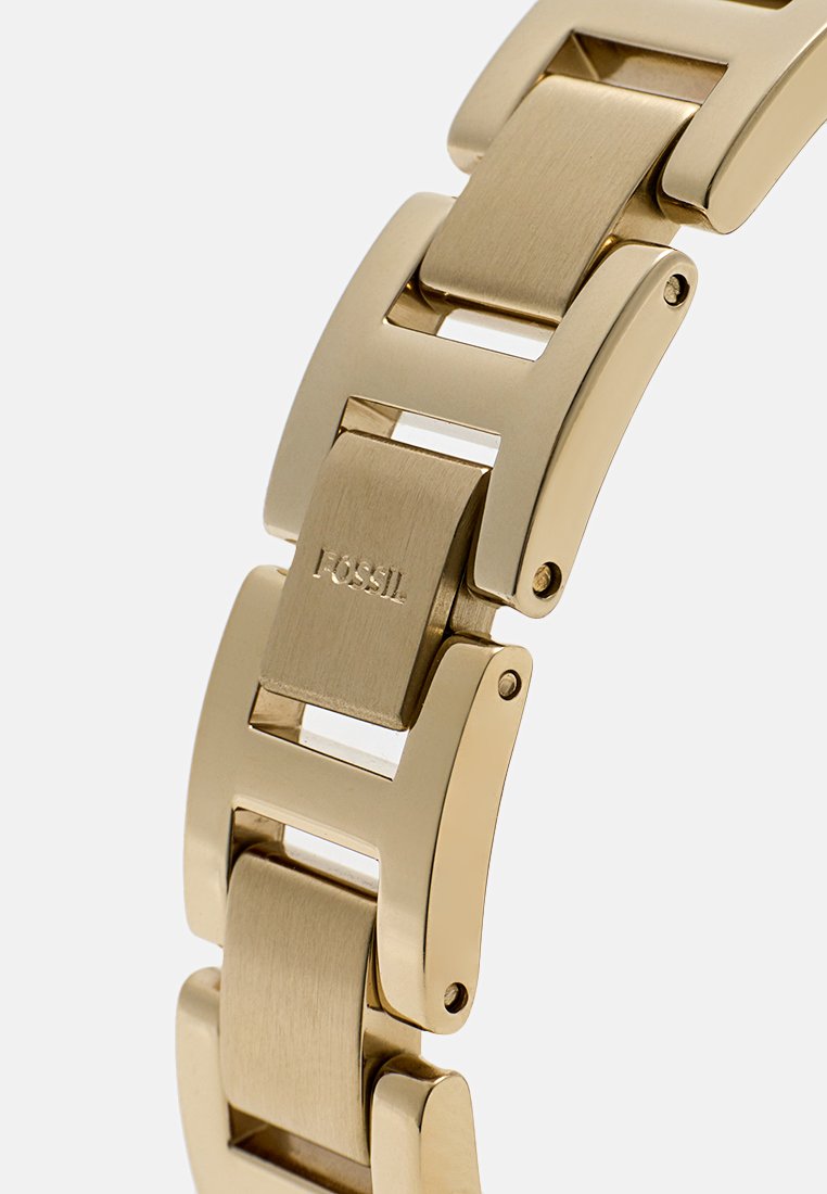 Bracelet en métal doré avec une finition polie. Comporte des maillons rectangulaires et un logo Fossil sur le fermoir. Texture lisse et design moderne.
