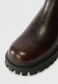 Καφέ δερμάτινη μπότα αστραγάλου με στρογγυλή μύτη, που διαθέτει υφή και παχύ μαύ�ρο λάστιχο με αυλακώσεις.