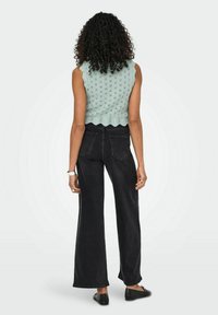 Mintgroene, gestructureerde gebreide mouwloze top met een geschulpte onderrand, gecombineerd met hoge zwarte wijde jeans en balletschoenen.