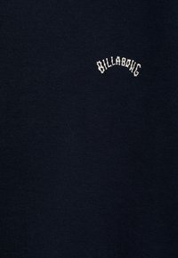 Felpa blu navy con texture morbida, caratterizzata da un logo "Billabong" ricamato di colore bianco a forma ad arco sul lato sinistro superiore.