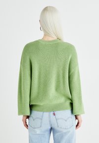 Grønn strikkegenser med en avslappet passform, ribbet tekstur, vide ermer og rund hals, kombinert med lyseblå jeans.