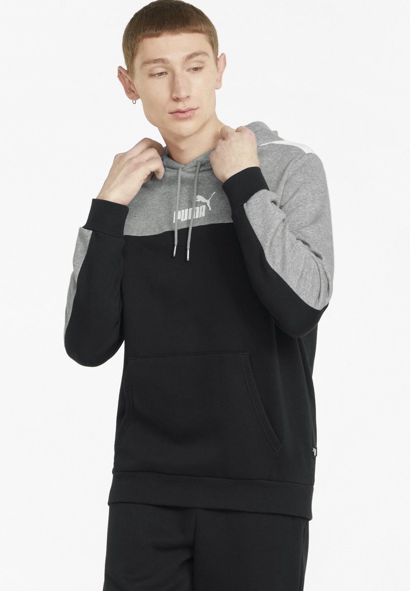Sudadera con capucha que tiene una sección superior gris y una sección inferior negra. Presenta un bolsillo tipo canguro y el logo de PUMA en blanco en el pecho.