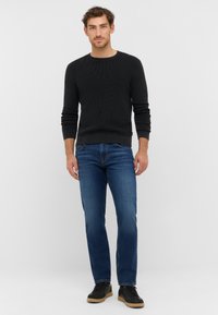 Pull en maille côtelée noire, ajusté aux poignets, associé à un jeans en denim bleu, coupe droite, porté avec des baskets noires, au design simple.