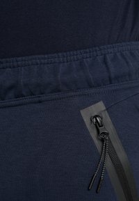 Marineblauwe sportbroek met een gestructureerde tailleband, voorzien van een zwarte, met rits gesloten zak,accentueert met rubberen rand. Glad weefsel, aansluitend ontwerp.