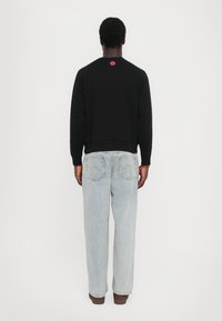 Svart hettegenser med rund hals og ribbestrikkede mansjetter, med en liten rød logo på baksiden. Kombinert med lyseblå rettlår jeans.
