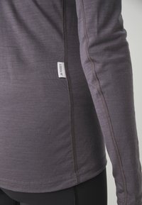 Long-sleeve shirt in dark gray fabric featuring flatlock seams and a branded tag. Smooth texture with a fitted design.
