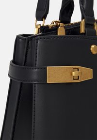 Czarna skórzana torebka o strukturalnym designie, z złotymi akcesoriami i zapięciem na zatrzask. Faktura jest gładka, z subtelnymi detalami stębnowania.