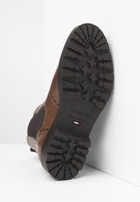 Semelle de botte en cuir brun avec une semelle extérieure en caoutchouc texturé et antidérapant. Comprend un logo de marque visible et un marquage de taille.