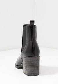 Stivale in pelle nera alla caviglia con un tacco grosso e rigato. Presenta un pannello laterale elastico e un piccolo tassello sul retro. Texture liscia.