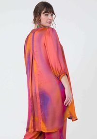 Satin tuniek in levendige roze, oranje en paarse tinten. Losse pasvorm, ballonmouwen en een gespleten rugdetail. Zachte textuur.