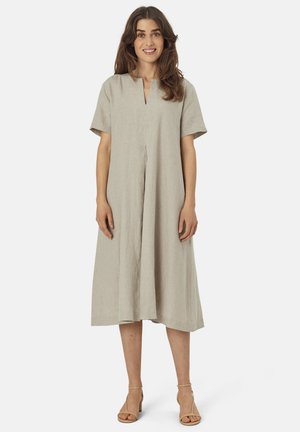 Beige linneskjorta med korta ärmar, V-ringning och en framtill veck, som når till mitten av vaden. Matchad med beige sandaletter med klack och remmar.