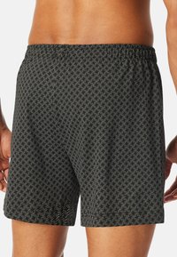 Black swim trunks with a geometric white pattern, elastic waistband, and a relaxed fit, showcasing a smooth, lightweight fabric texture.