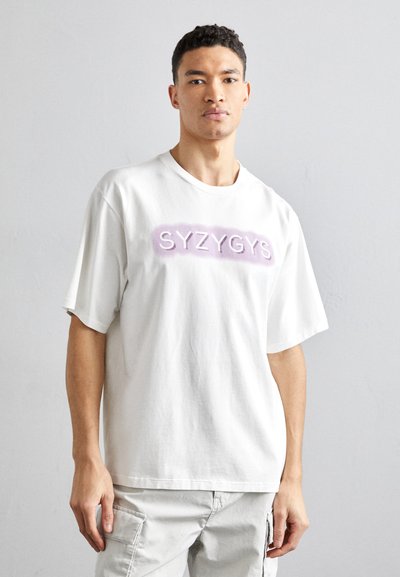 Tricou alb din bumbac, cu mâneci scurte, având un logo ridicat de culoare purpurie "SYZYGS" centrat pe față. Textură moale, croială lejeră.