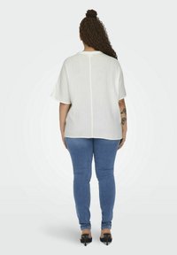 Hvid oversized skjorte med en tekstureret finish, rund halsudskæring og korte ærmer, parret med blå tætsiddende jeans og sorte hæle. 