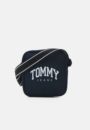 Borsa a tracolla in tessuto blu navy con logo bianco "TOMMY JEANS". Presenta una tracolla regolabile a strisce in contrasto e una chiusura a zip. Forma quadrata compatta.