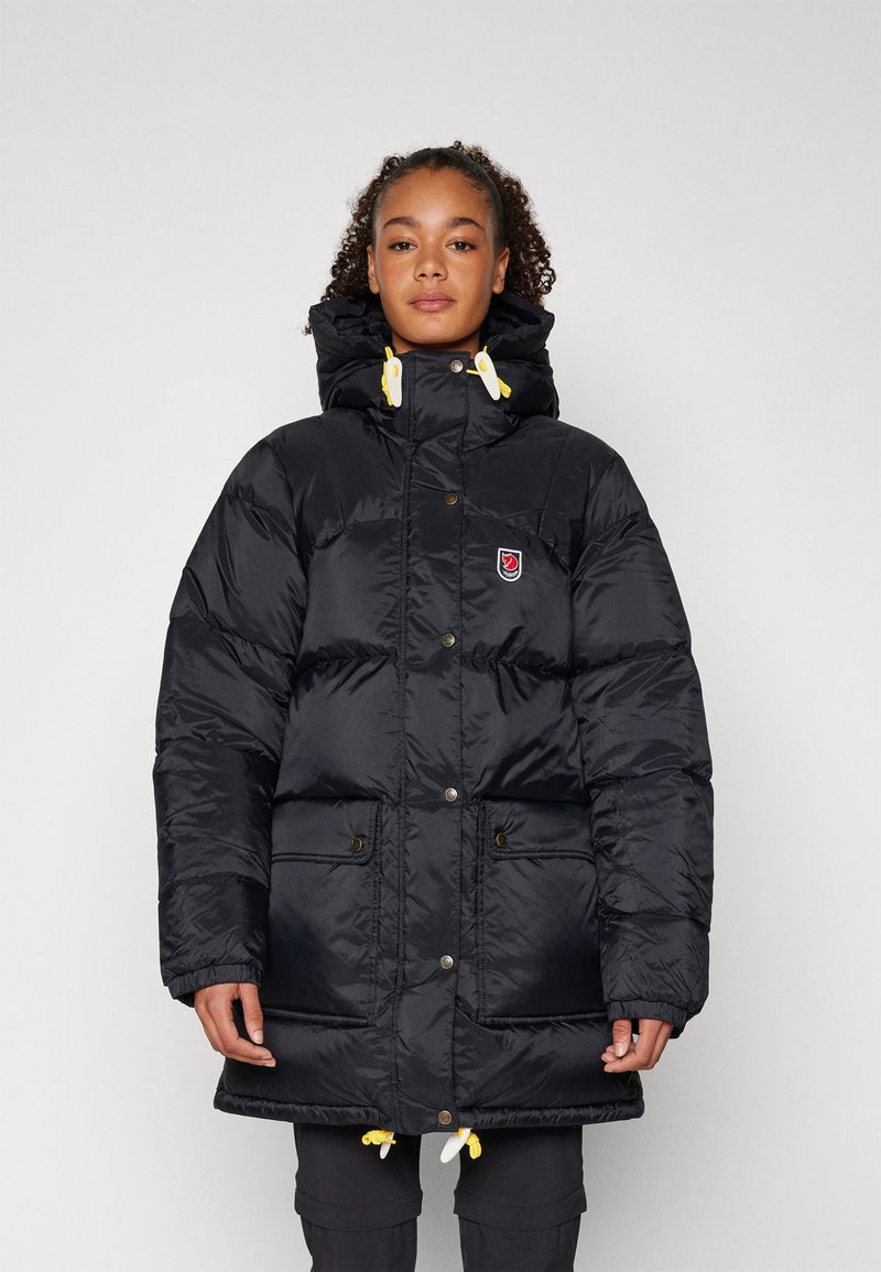 Black puffer jacket with a high collar, featuring yellow drawstring accents, snap buttons, and two front pockets. Made of glossy material.
