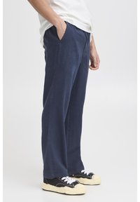 Pantaloni din in bleumarin, cu croială lejeră, prevăzuți cu buzunare laterale și textură netedă. Asortați cu adidași negri cu șireturi albe.