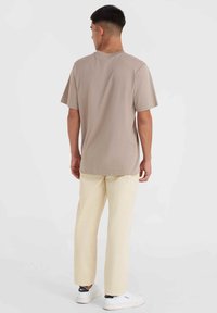 T-shirt en coton beige à manches courtes avec un col rond, coupe décontractée et texture lisse, associé à un pantalon droit jaune clair et des baskets.