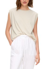 Paskowany bezrękawnik w jasnym beżu, wykonany z miękkiego materiału. Posiada luźny krój z wysokim dekoltem i minimalnymi szwami. W połączeniu z białymi spodniami.