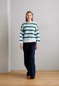 Gestreepte trui in teal, wit en donkergroen met brede mouwen, gedragen met donkere denim flare pants. Glad textuur, relaxed fit.