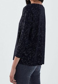 Maglietta nera a maniche lunghe, con un delicato motivo floreale grigio. Realizzata in tessuto morbido, con una vestibilità rilassata e scollo rotondo.