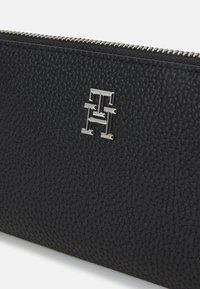 Black leather wallet featuring a textured finish and silver logo hardware. Zipper closure along the top edge. Compact and rectangular shape.