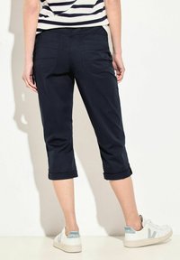 Navy cropped byxor med uppvikta nederkanter, två bakfickor och en slät textur, matchade med vita sneakers med blå accenter.