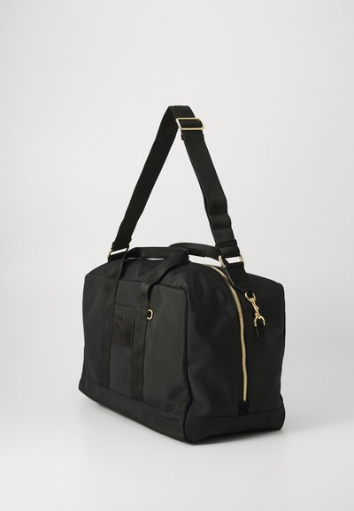 Geantă duffel neagră cu fermoar aurit, mânere duale de transport și curea de umăr ajustabilă. Textură netedă, formă dreptunghiulară, design minimalist.