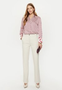 Camicia a maniche lunghe con bottoni in un motivo geometrico rosso e bianco, abbinata a pantaloni su misura color crema e tacchi beige chiaro.